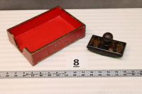 Red painted box with gold design and ink blotter with black lacquer and gilt figures next to measuring tape for scale.