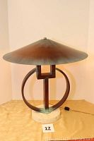 Front view of the lamp showing the large conical metal shade, sculpted circular and square metal elements, and round marble base.