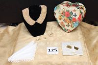 Wide shot of the entire lot showing the pearl collar on a black stand, three white lace-trimmed handkerchiefs, four pairs of earrings including pierced drop pearl and screw-back pearl earrings, a pearl lapel pin, and a floral heart-shaped box.