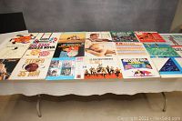 Wide view of about 19 vinyl record albums spread on a table showing various album covers with diverse musical styles.