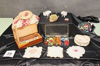 Photo showing the complete lot with pin cushions, sewing box, sewing bag, and other items arranged on black satin cloth backdrop.