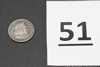 Silver half dollar coin placed on a black background with a white number card "51"