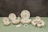 Full set of plates, cups, vase and small dish arranged on green surface against dark backdrop.