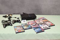 Sony PlayStation 2 console with 2 wired controllers and 8 game cases arranged on a table.