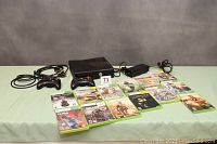 Full lot overview showing console, two controllers, power supply and cables, and 13 games laid out on a green surface.