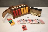 Full view of poker chip holder with colorful poker chips in stacks, a box of white chips, and 12 decks of cards spread out on table.