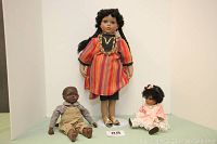 Photo of all three African-American dolls: the 20-inch girl doll in colorful striped dress standing, 7-inch pink dress girl doll sitting, and 11-inch boy doll seated.