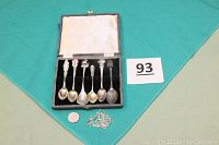 Photo showing six souvenir spoons inside an open lined box alongside crystallized silver pieces and a quarter for scale.