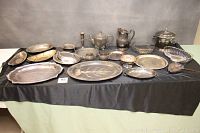Full view of all silver plated serving pieces on a table with black cloth background