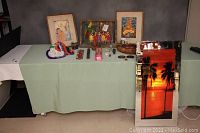 Full view of the table showing all items arranged including framed artworks, cloth dolls, coasters, wooden items, and the lighted mirror with sunset scene.