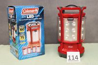Photo of the Coleman LED lantern standing next to its original blue branded box, showing front view of the main lantern body and packaging.
