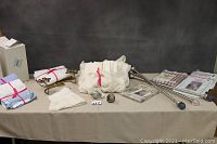 View of window treatment items on table including folded sheer panels, brass brackets, curtain rods with various finials, and packaged panels.