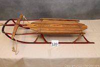 Full side view of wooden sled showing red metal runners, wooden slats, and attached rope handle
