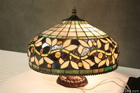 Photo of Tiffany style lamp lit on table showing stained glass shade and ornate base from front angle.