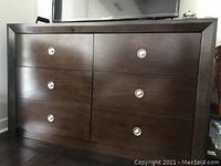 Photo of brown 4 drawer solid wood dresser showing front view with metal hardware handles on drawers.