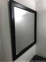 Square mirror hung on wall showing dark wood frame and clear glass surface.