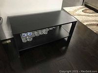Image shows a rectangular black-brown IKEA Lack coffee table in a room setting on a dark floor with several water bottles on the lower shelf.
