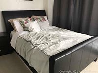 Queen bed with brown faux leather upholstered frame, box spring visible, mattress with bedding