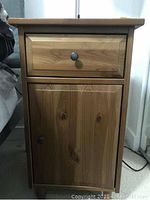 Front view of IKEA pine wood bedside side table with single drawer and cabinet door, showing natural wood grain and metal round knobs.