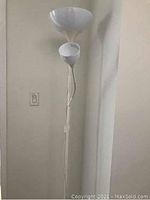 Full view of the white standing floor lamp showing both the main light and the attached reading light, with power cord and inline switch visible.