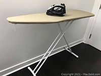 Photo of a black Sunbeam iron resting on a beige-covered ironing board with white folding metal legs.