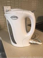 White plastic Traditions electric kettle on kitchen counter with cord plugged in, showing handle, water level gauge, and spout.