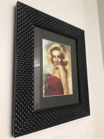 Angled photo of framed Marilyn Monroe portrait showing black woven-style frame and grey mat