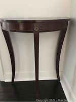 Front view of a half round table with three curved legs and a central decorative accent on the apron, dark polished wood finish.