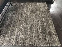 Photo showing the entire brown shag rug lying flat on a wooden floor, with sunlight highlighting its textured, thick pile.