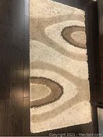Top view of rug showing cream, light brown and brown swirl pattern on dark floor