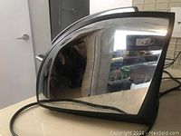 Side profile of the toaster showing the shiny, reflective stainless steel surface with some smudges and black plastic trim.