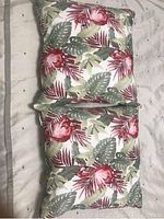 Two pillows stacked vertically showing their floral and leaf pattern fabric in red, green, and white colors on a light background.