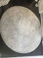 Full view of beige round rug showing the plush texture and a small damaged area near center.