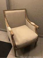 Front angle view of the wooden frame upholstered accent chair showing beige upholstery and carved arms.
