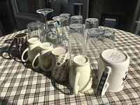 Photo showing arrangement of mugs and glasses placed upside down and upright on a plaid tablecloth.