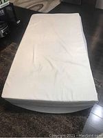 Single mattress with white memory foam topper cover on top in living room.