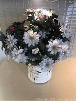 Front view of a white ceramic vase with a pink and green floral pattern containing an arrangement of white and small red artificial flowers with green leaves.
