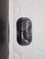 Close-up image of the Divine Sleep Ultra Sleep mattress brand tag sewn into the white surface with quilted pattern.