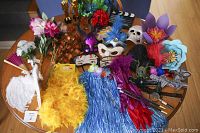 Wide view of assorted photo booth props and costume items arranged on a wooden table, including wings, boas, skirts, masks, hats, flowers, and awards.
