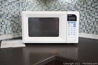 White Emerson microwave oven on kitchen countertop next to owner's manual.