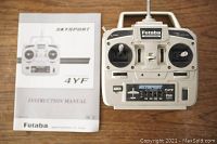 Top view of Futaba Skysport 4YF transmitter with instruction manual beside it on wooden surface.