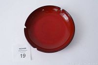 Top view of red ceramic ashtray showing gloss finish and three cigarette rests with small chip on rim.