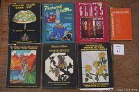 Overview of seven stained glass pattern books with colorful covers depicting various stained glass themes, arranged in two rows on a wooden floor.