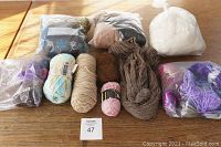 Photo showing yarn skeins in various colors plus three bags of felting wool on wooden table.