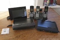 Photo showing all items arranged on a wooden surface including three Panasonic cordless phones, two Philips car DVD players and one digital photo frame.