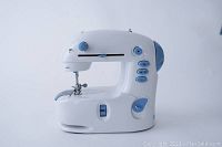 White mini sewing machine shown from the side, featuring blue control knobs and buttons.
