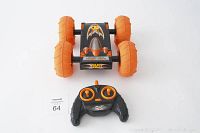 Photo showing the black and orange stunt car with large orange rubber tires and the remote control transmitter underneath it on a white background