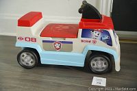 Side view of toddler-sized ride-on car with Paw Patrol decals, showing red seat and wheels.