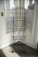 Front view of the black metal card rack standing tall with multiple wire baskets for holding postcard-sized items.