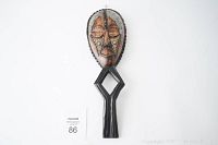 Front view of hand carved African mask showing the elongated face with metal detailing and geometric shapes.